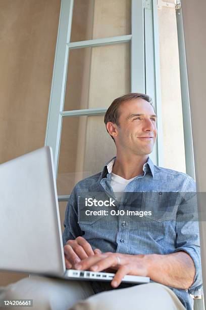Smiling Mid Adult Man Using Laptop Looking Through Window Stock Photo - Download Image Now