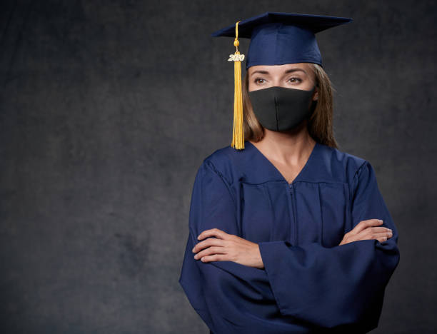 istock Young female graduate both hands on the side celebrating her university degree wearing blue cap and gown also wearing black mask 1242066651