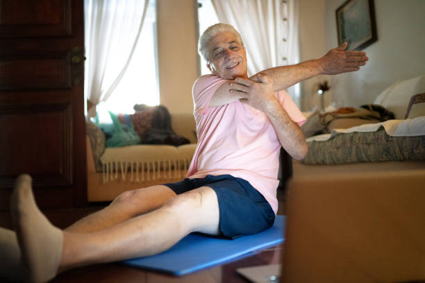 istock Senior man watching gym class on laptop and doing exercises at home 1242066665
