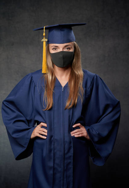 istock Young female graduate both hands on the side celebrating her university degree wearing blue cap and gown also wearing black mask 1242068075