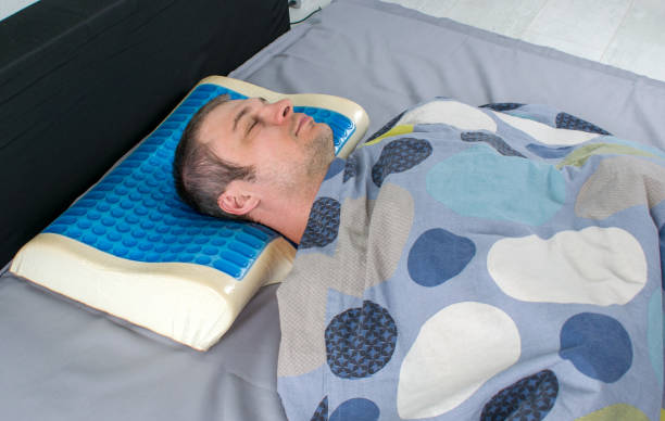 Young man sleeps in bed at home on latex pillow with memory and cooling effect. Men lying on bed with orthopedic pillow. Healthy posture concept. Latex pillow with memory foam effect, hydro gel layer. Medical treatment pillow for sleep under the head with a recess under the neck. cooling rack stock pictures, royalty-free photos & images