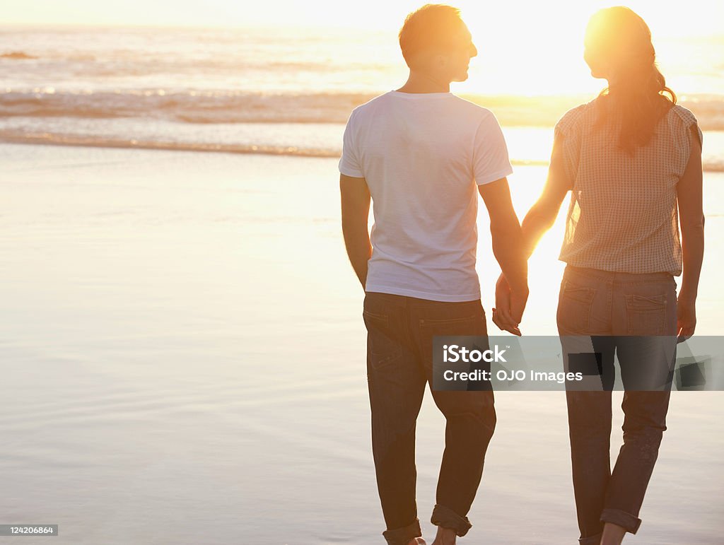 Vista posteriore di una coppia romantica a piedi alla spiaggia holding - Foto stock royalty-free di Due persone