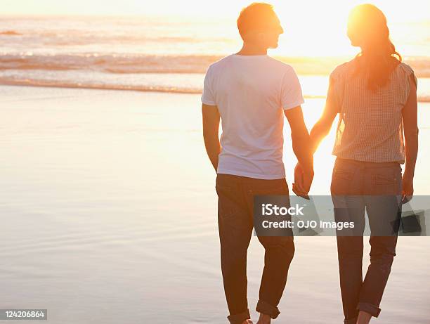 Vista Traseira De Um Casal Romântico A Caminhar Na Praia Segurando - Fotografias de stock e mais imagens de Duas Pessoas