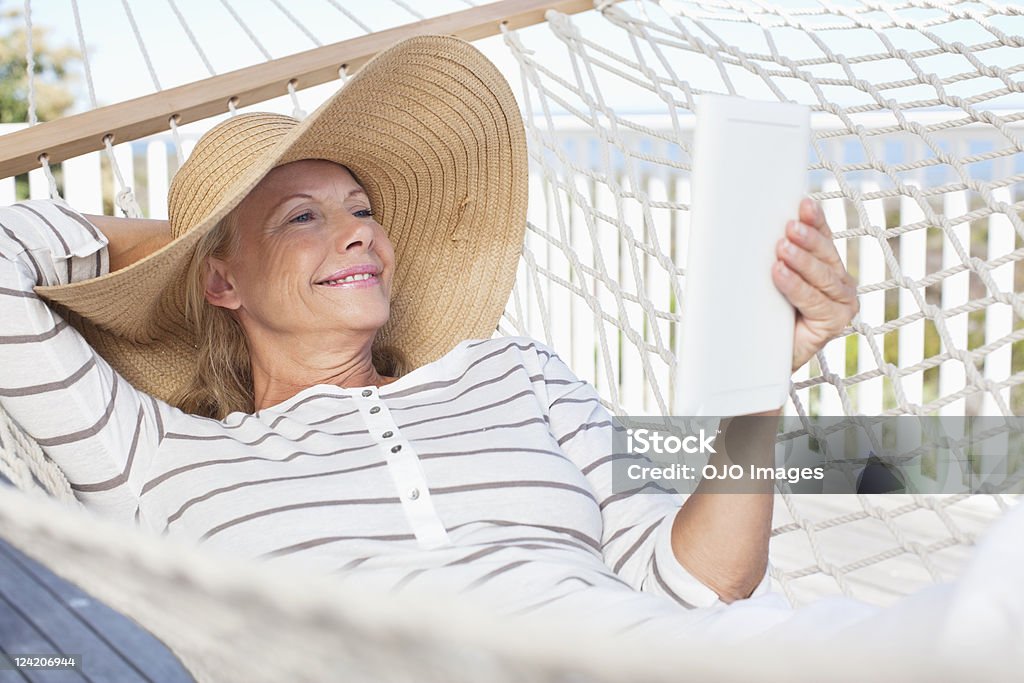 Femme d'âge mûr souriant à l'aide d'affichage électroniques dans un hamac - Photo de Hamac libre de droits