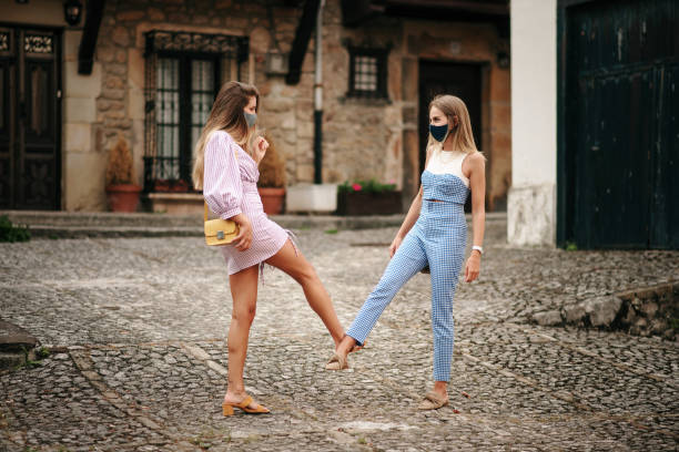 Two women greeting with their feet and wearing protective face masks during the COVID-19 pandemic