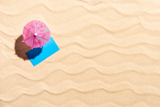 istock Sun cocktail umbrella and beach towel on hot sand 1242121649