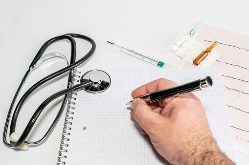 Hand of cardiologist doctor writing the diagnosis on block notes after seeing the electrocardiogram. High quality photo