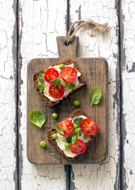 Open sandwiches with cream cheese, cherry tomatoes, green peas and basil close up stock photo