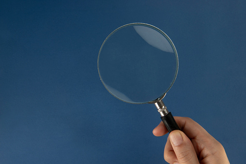 Hand holding magnifying glass, navy blue background.