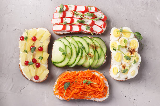 istock Five sandwiches on toast with fresh carrots, cucumbers, pineapple, red currant, crab sticks and quail eggs with peas microgreens on gray background. View from above 1242146018