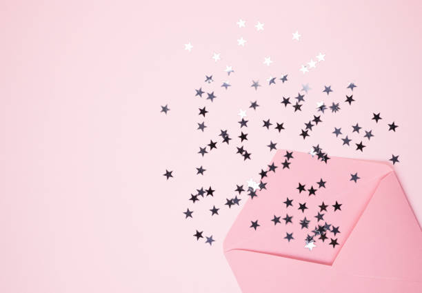 istock Shiny confetti stars pours from a pink envelope on a pastel pink background, top view 1242153627