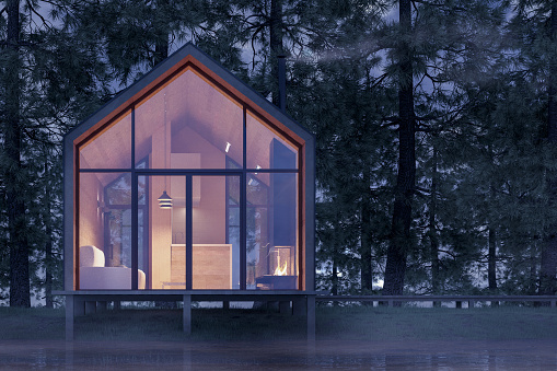 Secluded tiny house on the sandy shore of a lake with fog in a coniferous forest in the cold night light and with warm light from the Windows. Stock 3D illustration