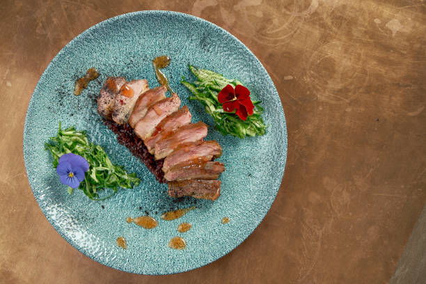 istock Appetizing baked duck breast with black risotto and cucumber salad on a blue ceramic plate on a metal, copper background. Restaurant serving 1242177191