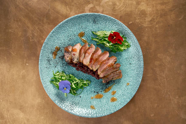 istock Appetizing baked duck breast with black risotto and cucumber salad on a blue ceramic plate on a metal, copper background. Restaurant serving 1242177715