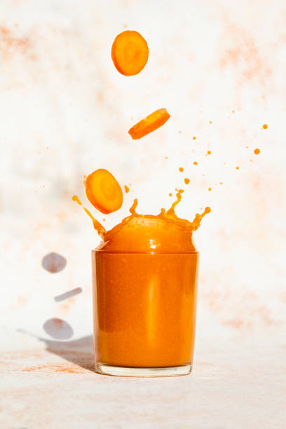 Fresh carrot juice splash in glass on a light background stock photo