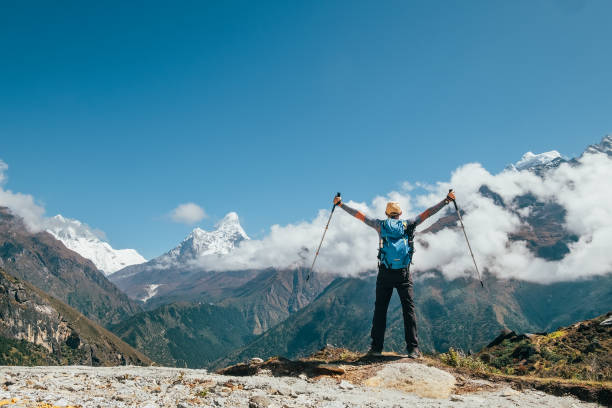 istock Active vacations concept image. Young hiker backpacker man rising arms with trekking poles enjoying the Thamserku 6608m mountain during high altitude Acclimatization walk. Everest Base Camp route,Nepal. 1242242774