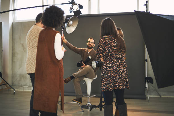 istock Young handsome bearded educator showing to his multicultural attendees how camera works. Photo studio interior. 1242244222