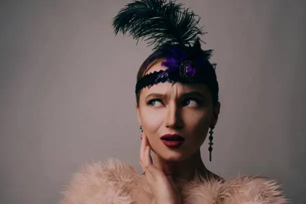 Photo of Girl in the 90s style, chicago style. Hat, headband with decorative feathers on the head. Incredible jewelry, long earrings with diamonds, coquette. Surprised looking away