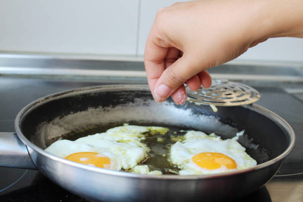 台所で卵を調理するために塩を追加する女性の手 - 塩をふる ストックフォトと画像