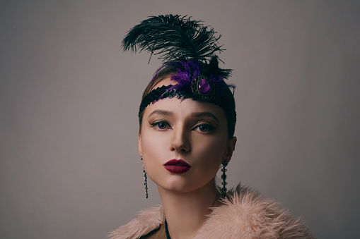 Girl in the 90s style, chicago style. Hat, headband with decorative feathers on the head. Incredible jewelry, long earrings with diamonds, coquette.