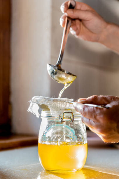 Man on Domestic Kitchen Counter with Accuracy Filtering Froth from Melted Butter for Making a Perfect Ghee Man on Domestic Kitchen Counter with Accuracy Filtering Froth from Melted Butter for Making a Perfect Ghee ghee stock pictures, royalty-free photos & images