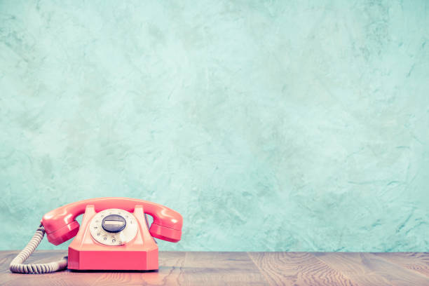 telefone rotativo rosa desatualizado retrô em frente de mesa de madeira texturizado fundo de parede de concreto aquático. foto filtrada do estilo antigo vintage - customer service representative on the phone retro revival office - fotografias e filmes do acervo