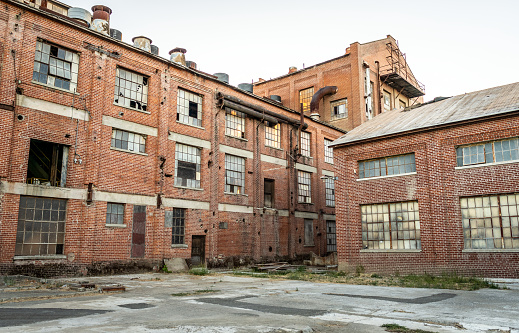 Abandoned multi-story brick factory building with broken glass windows.