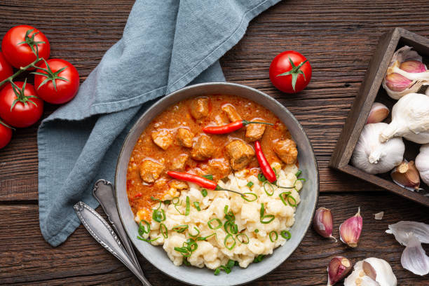 Hot pork goulash with chili, tomato and pepper, served with boiled dumplings topped with spring onion greens stock photo
