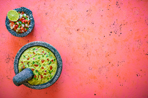 Guacamole Mexican avocado recipe with pico de gallo sauce in stone molcajete on coral pink background