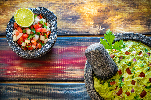 Guacamole with avocado and Pico de Gallo sauce Mexican recipes in stone molcajete on colorful grunge wooden backgrund rustic