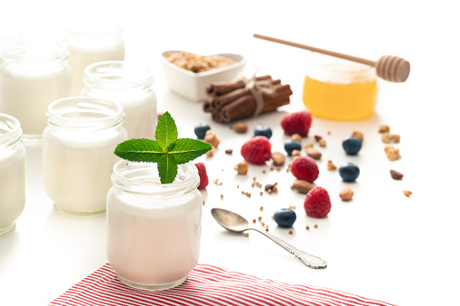 Homemade yoghurt yogurt in glass pots with mint leaves berries granola and honey isolated on white background