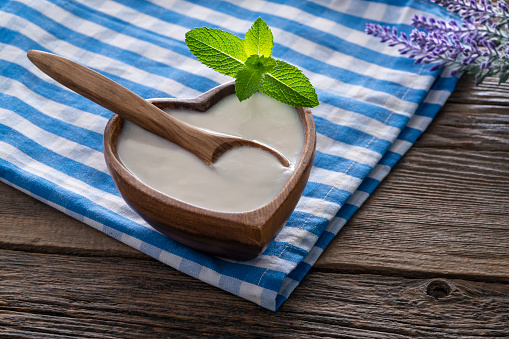 Homemade yogurt heart shape wooden bowl with mint leaves and glass container on rustic wooden board table for healthy breakfast