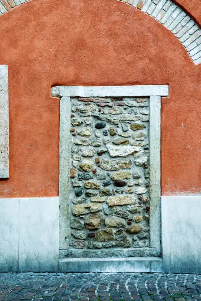 A bricked-up door on the orange wall of an old building with architectural details, Italy