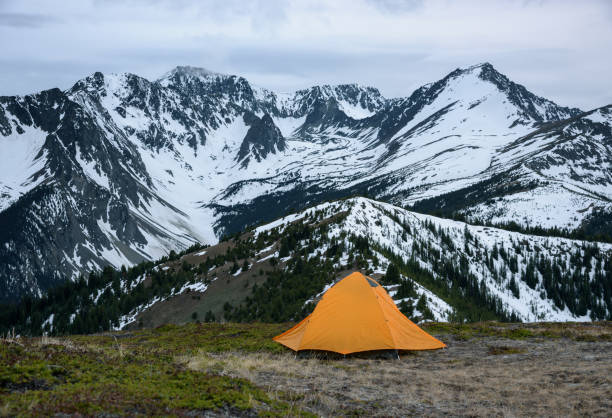 istock An orange tent pitched in front of a snowy mountain range. 1242394624