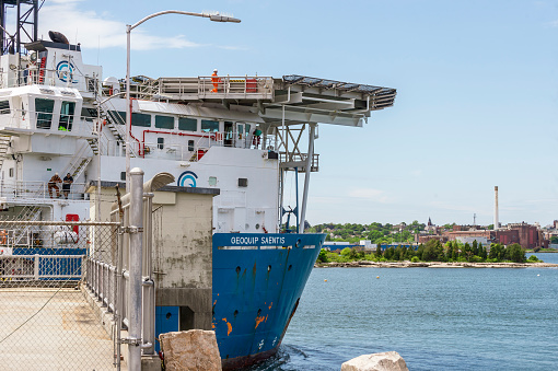 New Bedford, Massachusetts, USA - June 2, 2020: Crewman walking alongside helipad over boat's bridge as drilling vessel Geoquip Saentis transits hurricane barrier