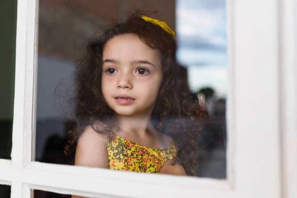 istock Little girl looking through the window glass 1242423086