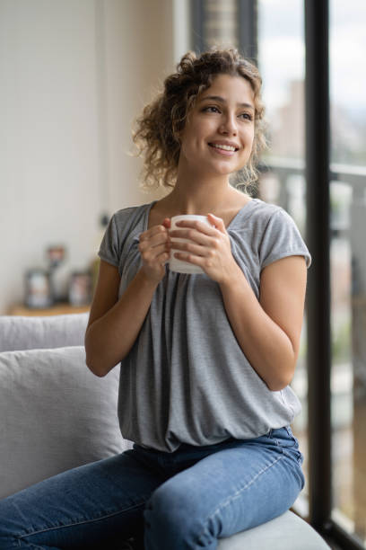 istock Pensive woman at home drinking coffee and looking happy 1242508937