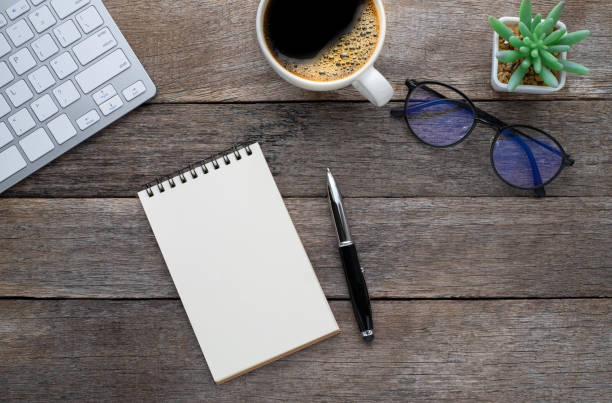 istock Top view from above of Blank open notebook, keyboard with glasses and coffee cup on wood table background. Workplace creative at home. Flat lay, Business-finance or education concept with copy space. 1242520936