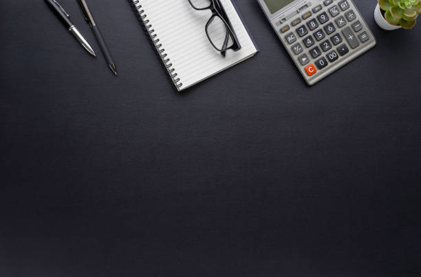 istock Workspace in office with black table. Top view from above of notebook with pen and glasses. Desk for modern creative work of designer. Flat lay with blank copy space. Business and finance concept. 1242520939