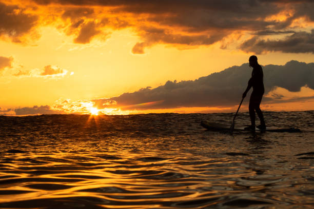 Stand Up Paddle Boarding In Japan at Sunrise and Sunset a solo rider keeping fit & healthy on the Pacific Ocean in a black wetsuit, also catching some large waves, The ocean is blue with a nice sky.