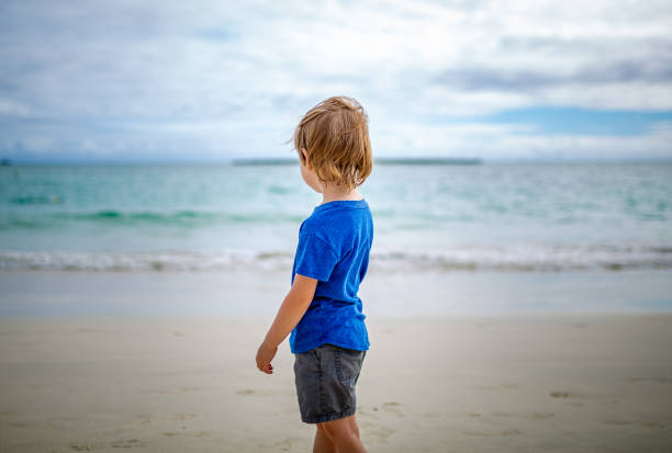 istock Young boy stares out at the ocean from the beach 1242558207