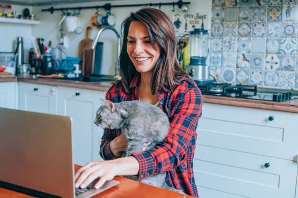Woman holding a cat and using laptop.
