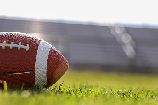 Football on grass stadium on college or high school campus. Bleachers background. No people.  Daytime.