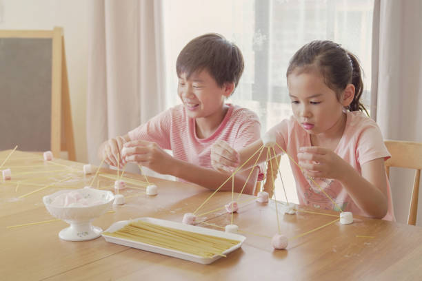 Mixed race young Asian children building tower with spaghetti and marshmallow learning remotely at home, STEM science, homeschooling education, Social distancing, isolation concept Mixed race young Asian children building tower with spaghetti and marshmallow learning remotely at home, STEM science, homeschooling education, Social distancing, isolation concept montessori education photos stock pictures, royalty-free photos & images