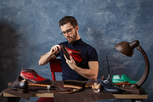 talented guy making shoes by hand in the shoe shop with blue wall