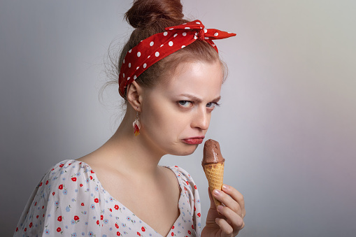 Frowning young Caucasian woman girl holding ice cream looks grumpy as if doesn't want to  share or angry, annoyed