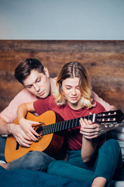 two friends playing the guitar at home