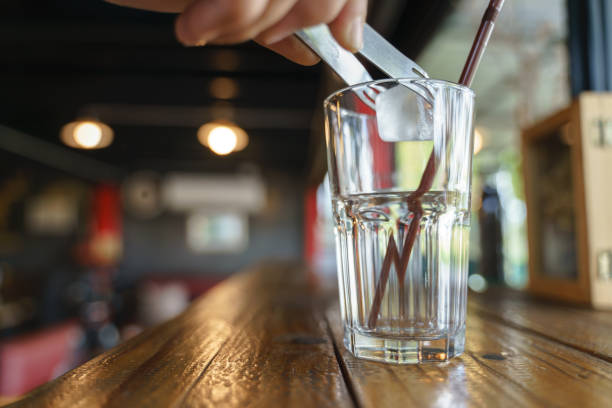 Filling the glass cup with ice by silver serving tongs in cafe