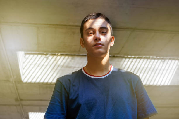 Teenager posing with light and shadow on his face in a low angle view as he looks down at the camera with a pensive expression