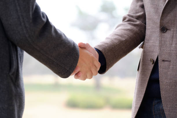 A Japanese man shaking hands outdoors.
